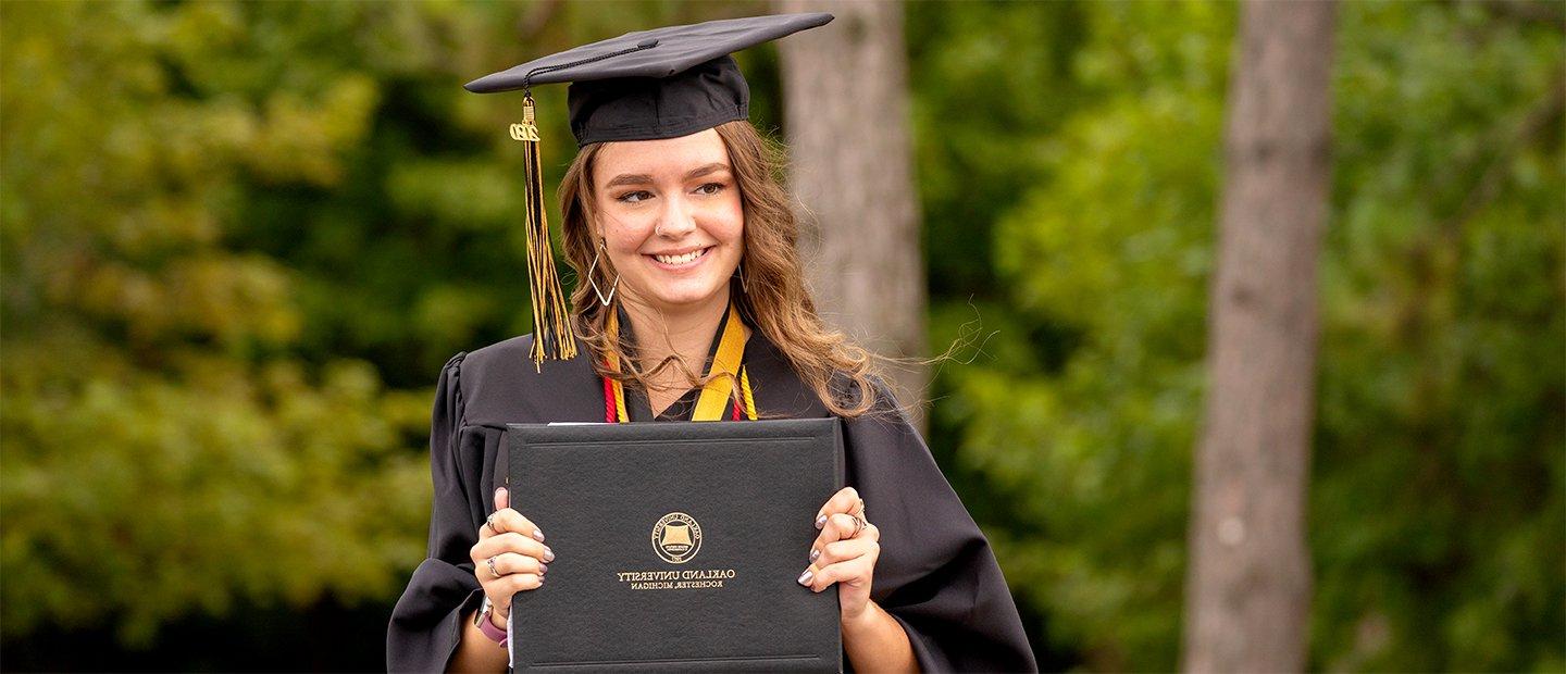 一位韦德体育app官网的女毕业生，戴着帽子，穿着长袍，手里拿着一张文凭.